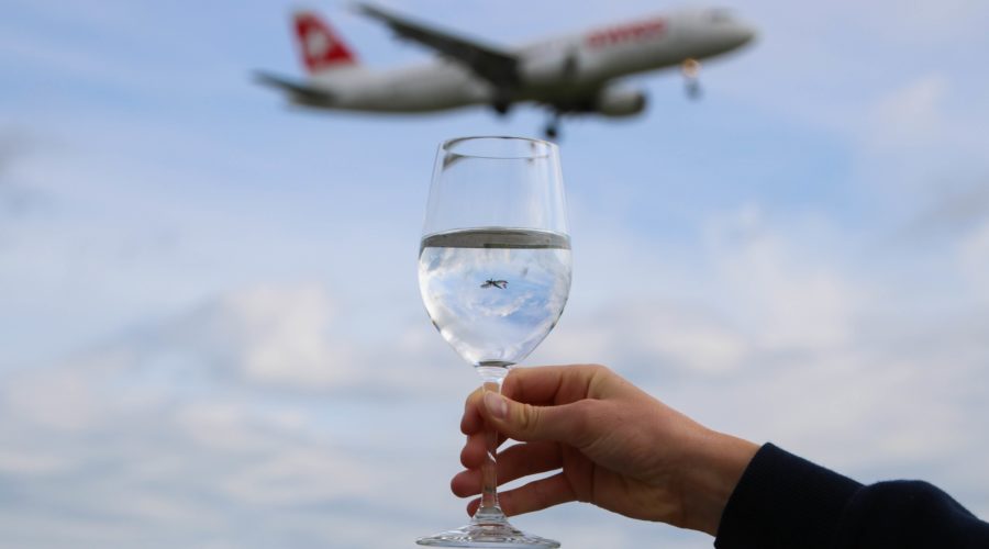 Mão segurando uma taça de vinho e um avião passando no céu ao fundo